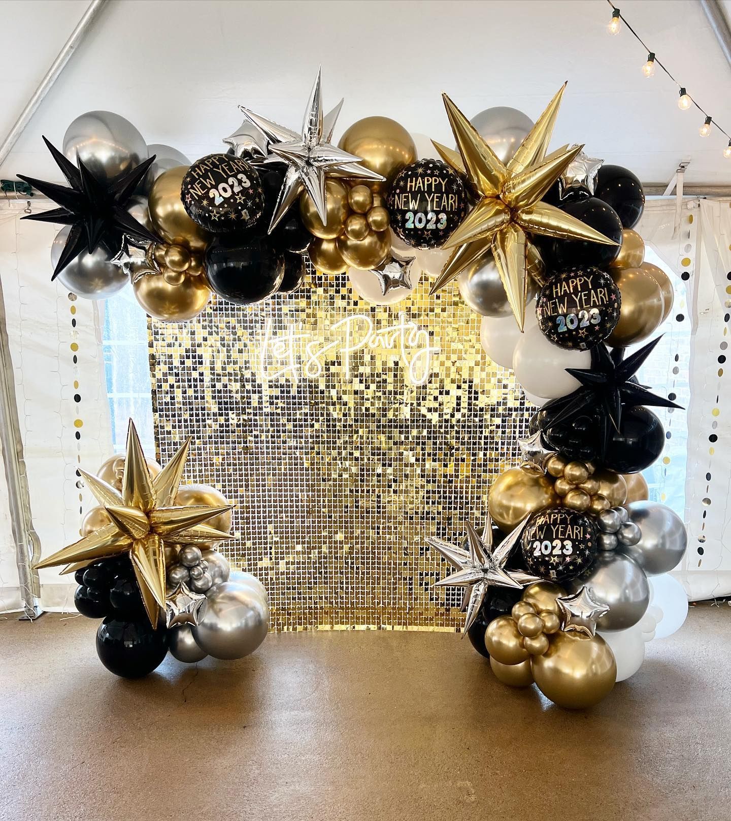 New Year's Eve balloon arch with gold, silver, and black balloons, star accents, and a gold sequin backdrop.