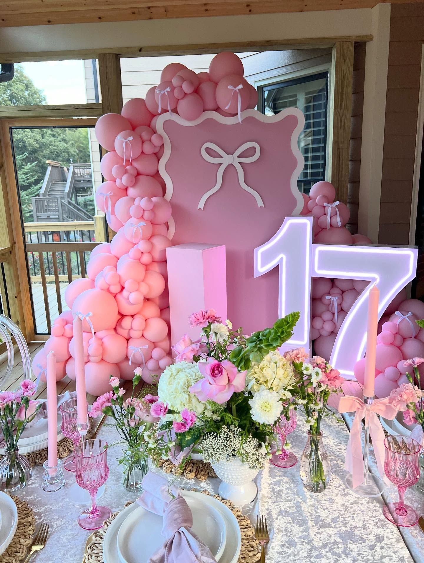 Pink 17th birthday party setup with balloon arch, floral arrangements, and light-up numbers.