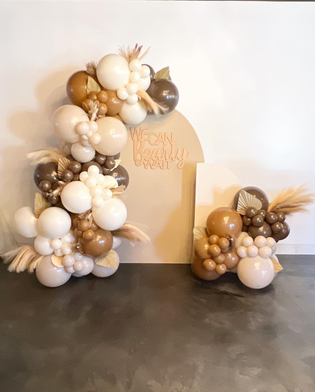 Balloon garland with tan, brown, and white balloons, and a backdrop, set indoors.