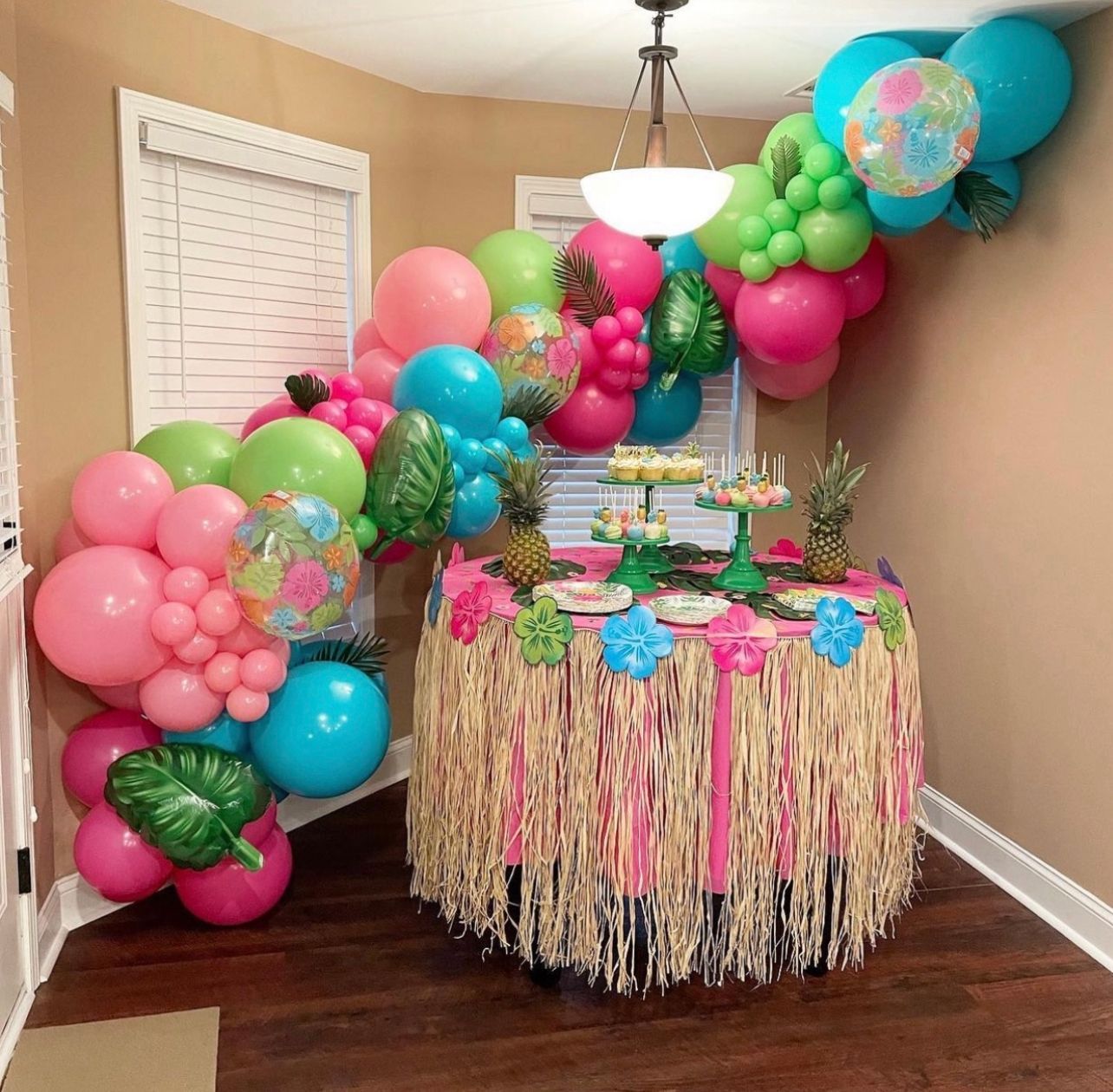 Balloon arch with tropical theme decorates a table with snacks and pineapples.