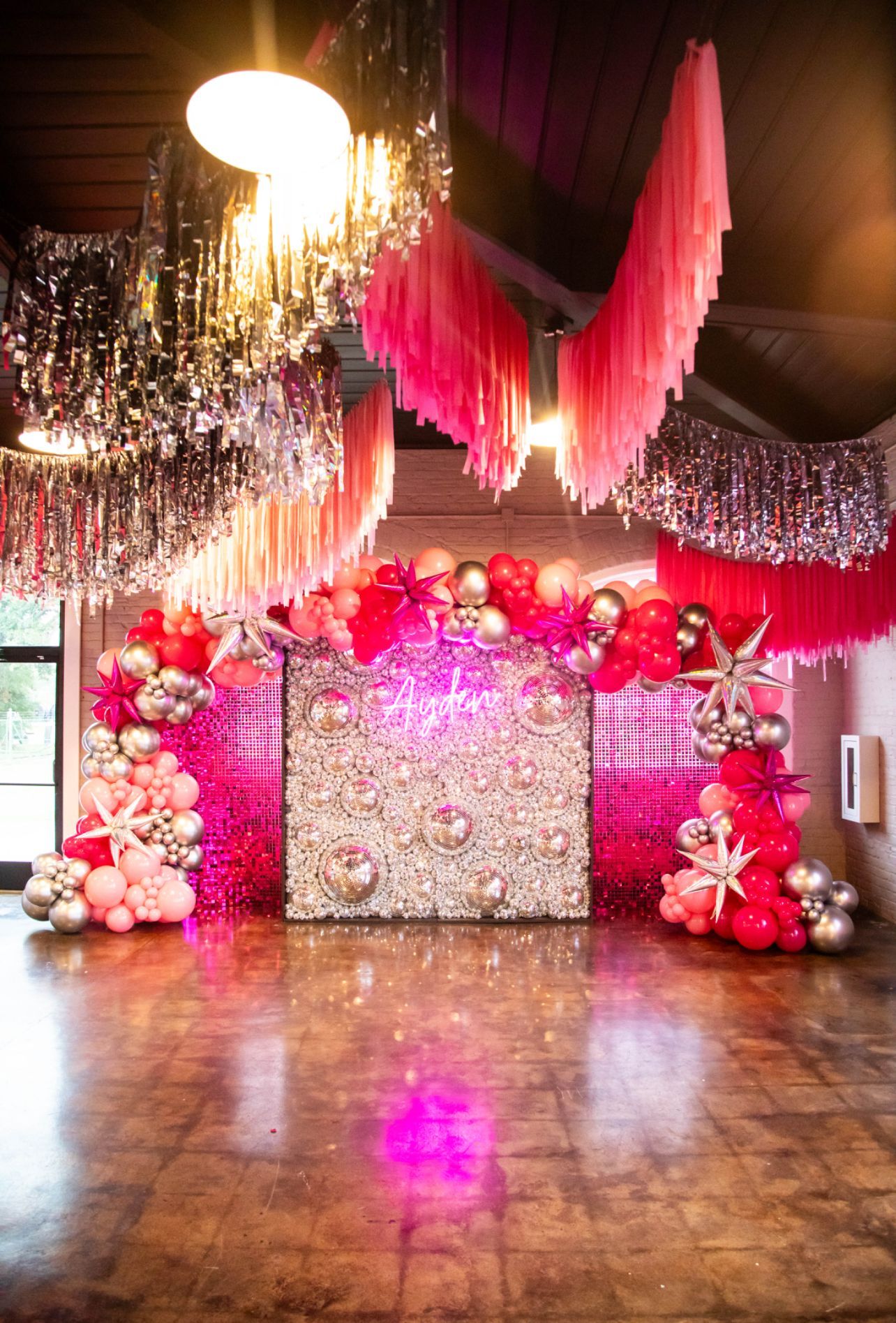 Festive party backdrop with pink, red, and silver decorations, balloons, and disco balls.