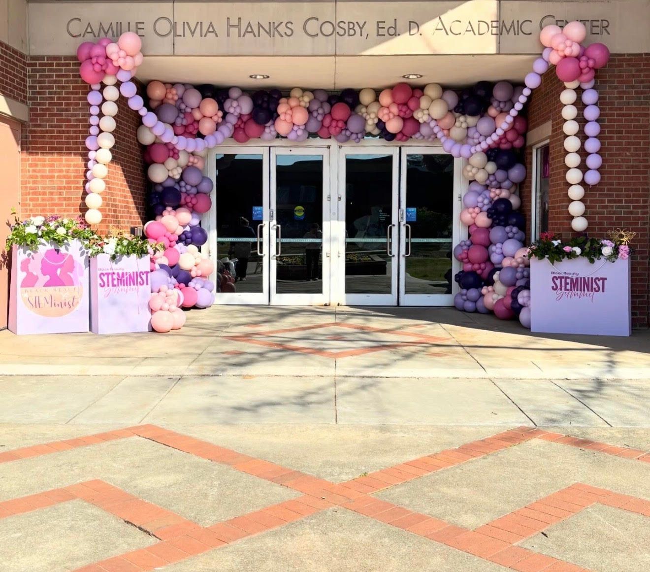 Entrance to the Camille Olivia Hanks Cosby Academic Center, decorated with a pink and purple balloon arch and event signs.