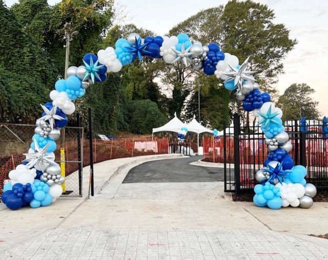 Balloon arch in shades of blue and silver, over a pathway and gate.