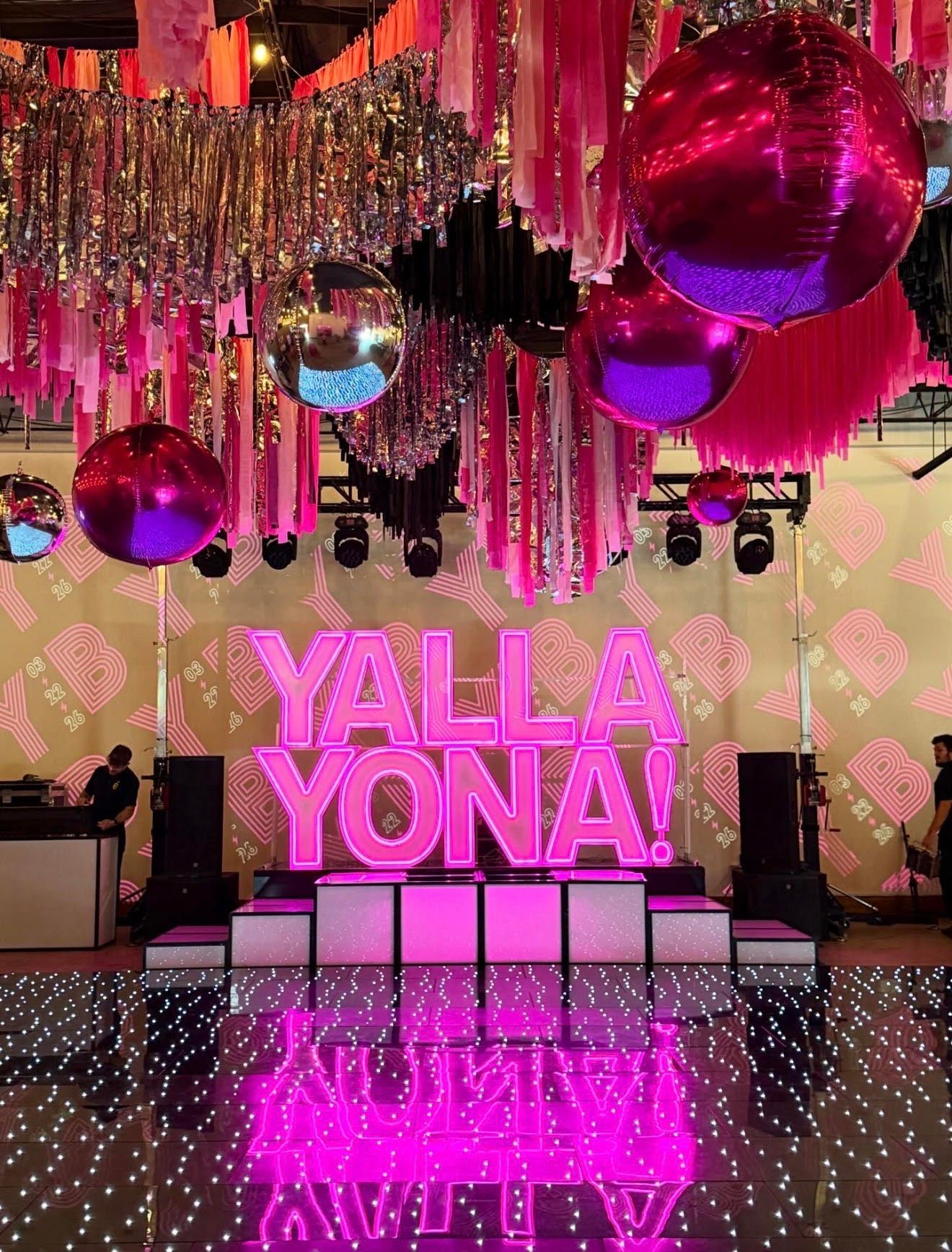 A vibrant event space features a large, glowing neon pink 