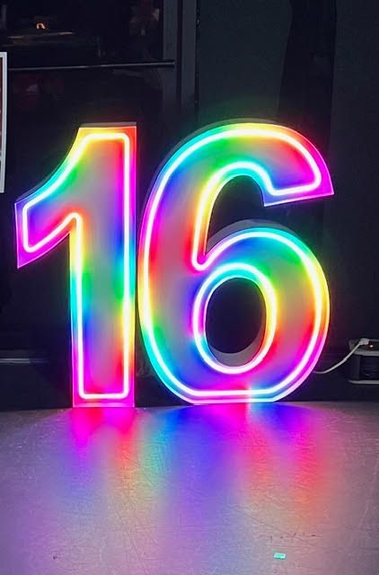 Neon sign displaying the number 16 in rainbow colors, casting colorful reflections on the floor.