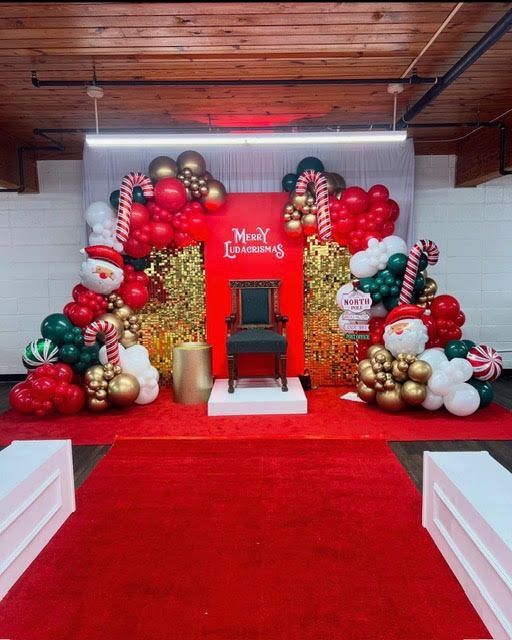 Christmas themed photo backdrop with balloons, chair, and red carpet.