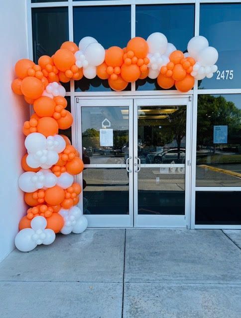Orange and white balloon arch over glass double doors of a building, with the number 2475 visible.