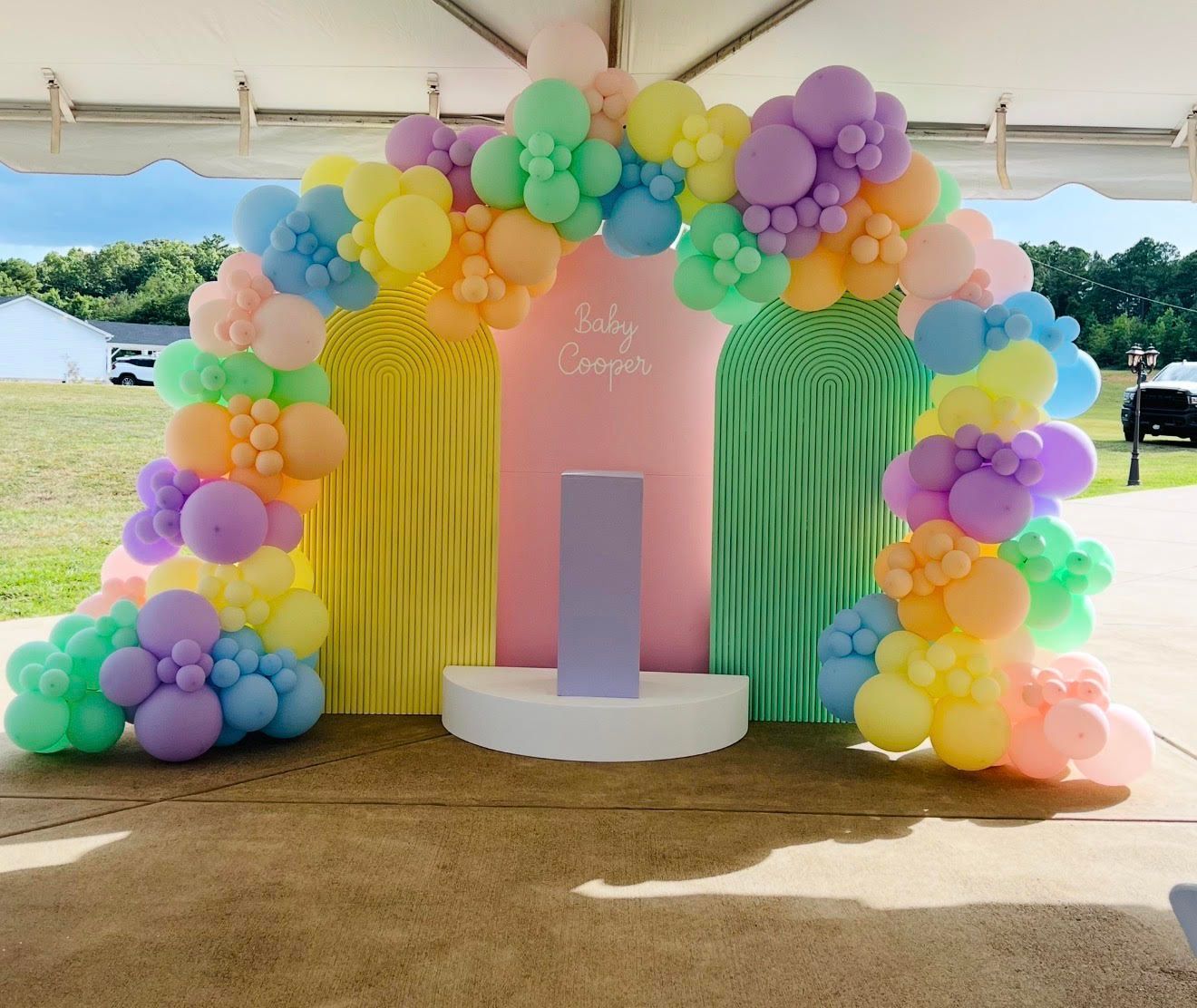 Pastel balloon arch over backdrop for a party, with the name 