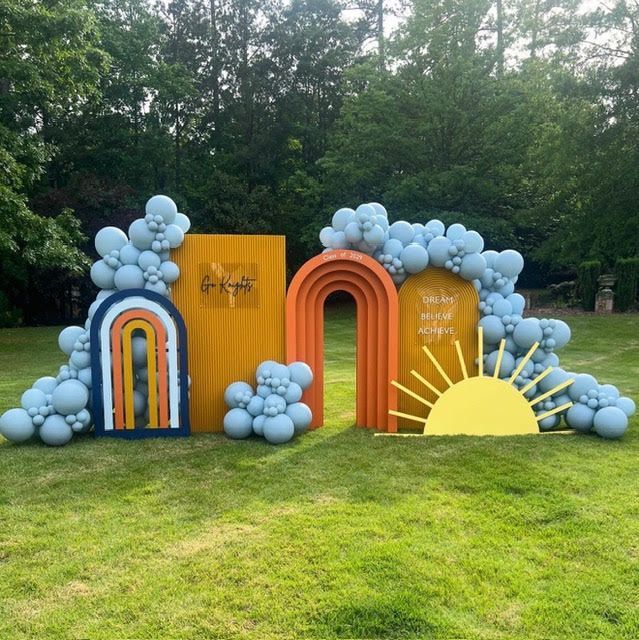Colorful outdoor party backdrop with arches, sun, and blue balloons.