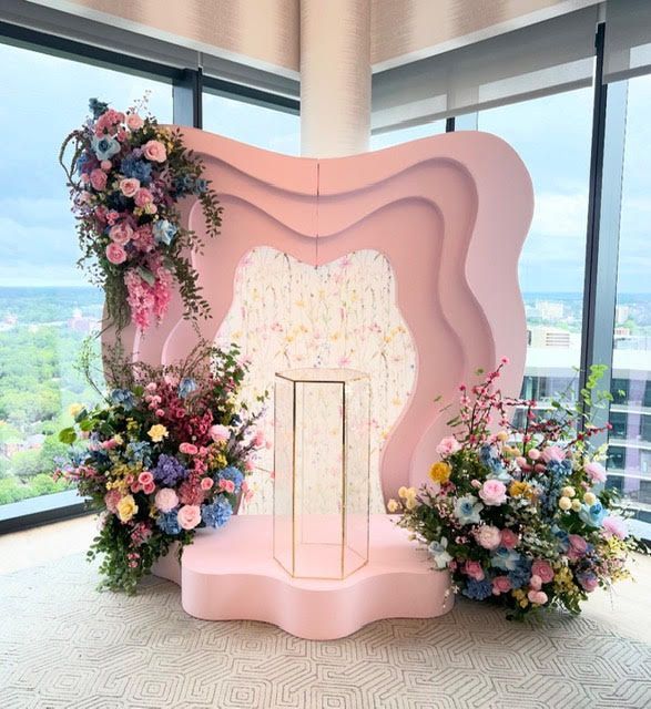 Pink floral backdrop with pedestal and floral arrangements, overlooking a city.