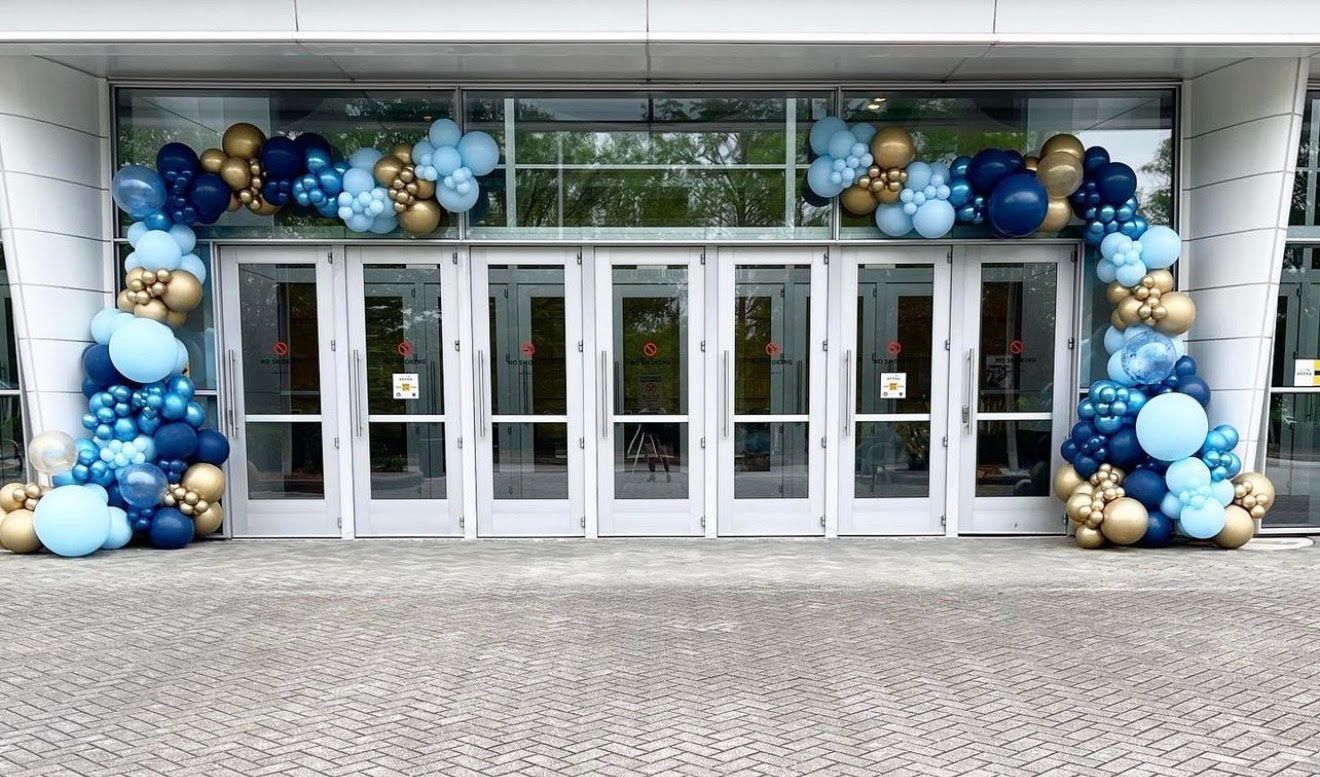 Entrance with white doors decorated with blue, light blue, and gold balloon arch.