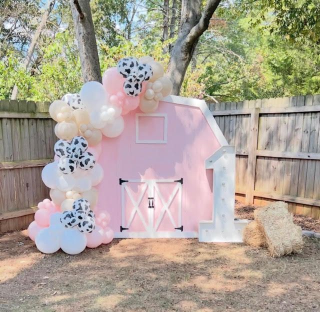 Pink barn backdrop with balloons and hay bale for a farm-themed birthday.