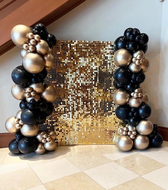 Gold sequin backdrop with black and gold balloon columns.