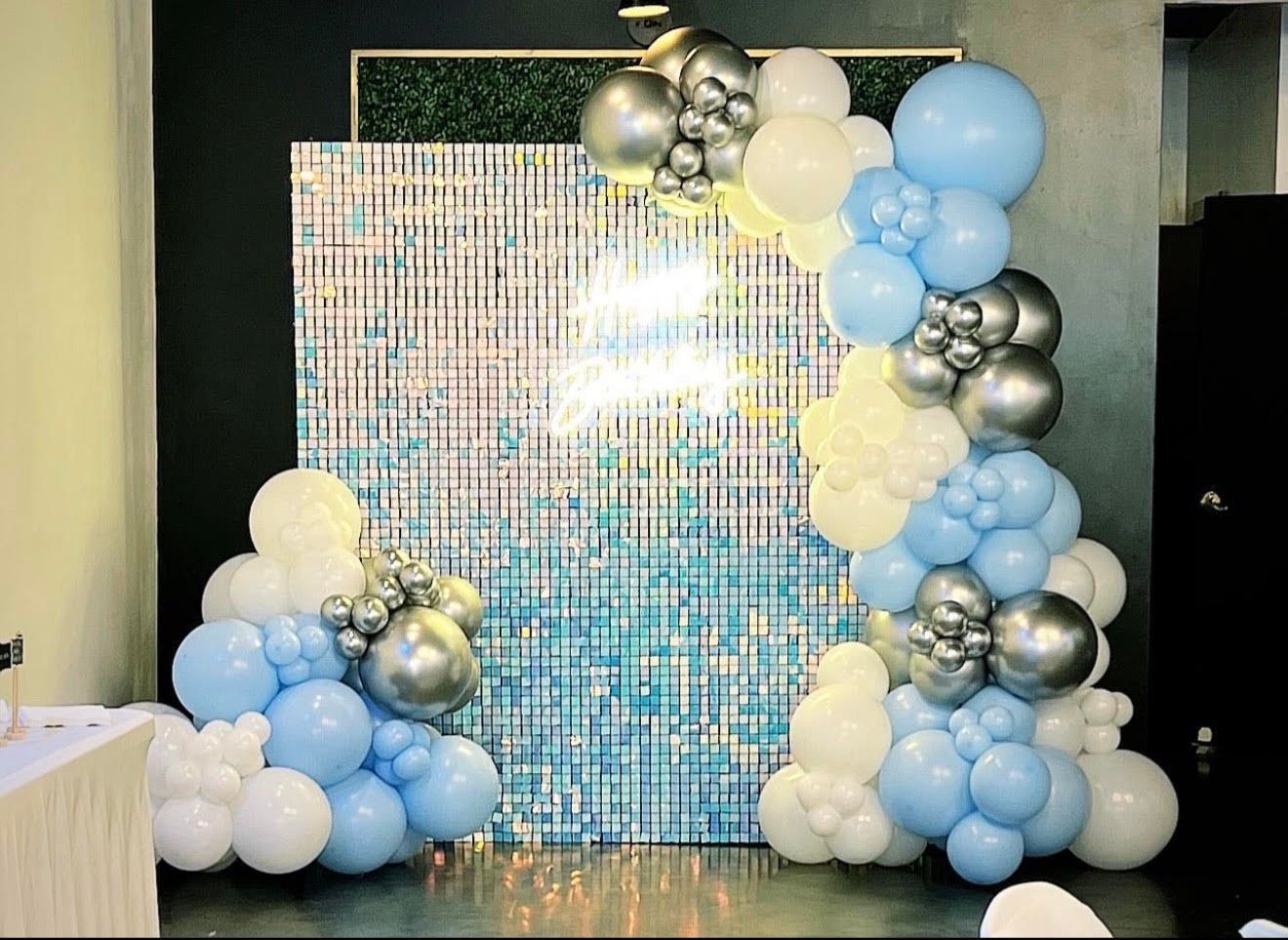 Balloon arch and clusters in blue, white, and silver framing a sparkly blue backdrop, possibly for an event.