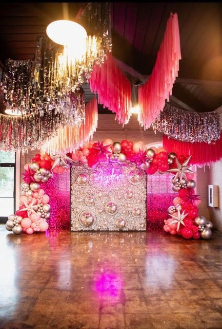 Pink and silver party backdrop with balloons, hanging decorations, and a glowing sign.