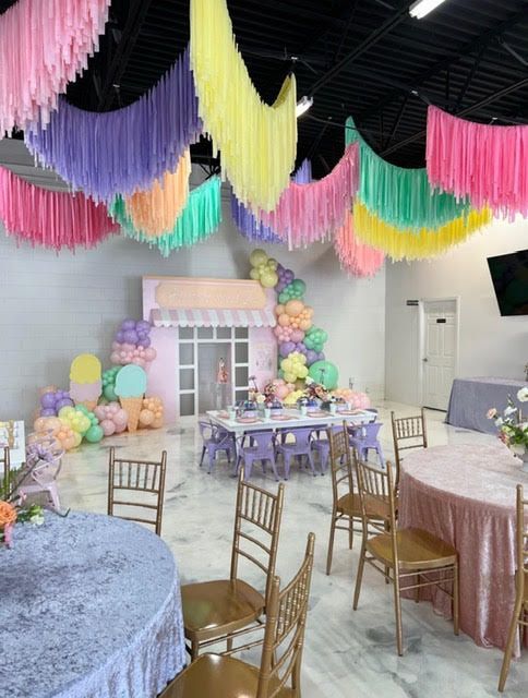 Pastel-colored party venue with draped ceiling decorations, tables, chairs, and a themed backdrop.
