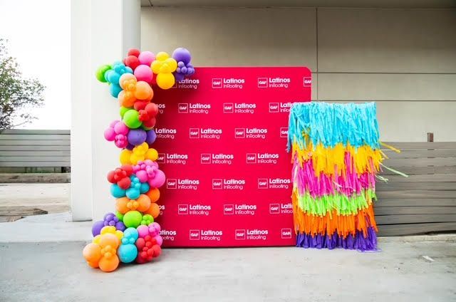 Balloon arch, backdrop, and fringed decoration in front of a building.