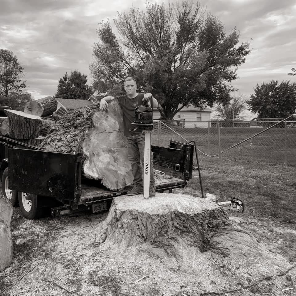 A black and white photo of a man standing on a tree stump
