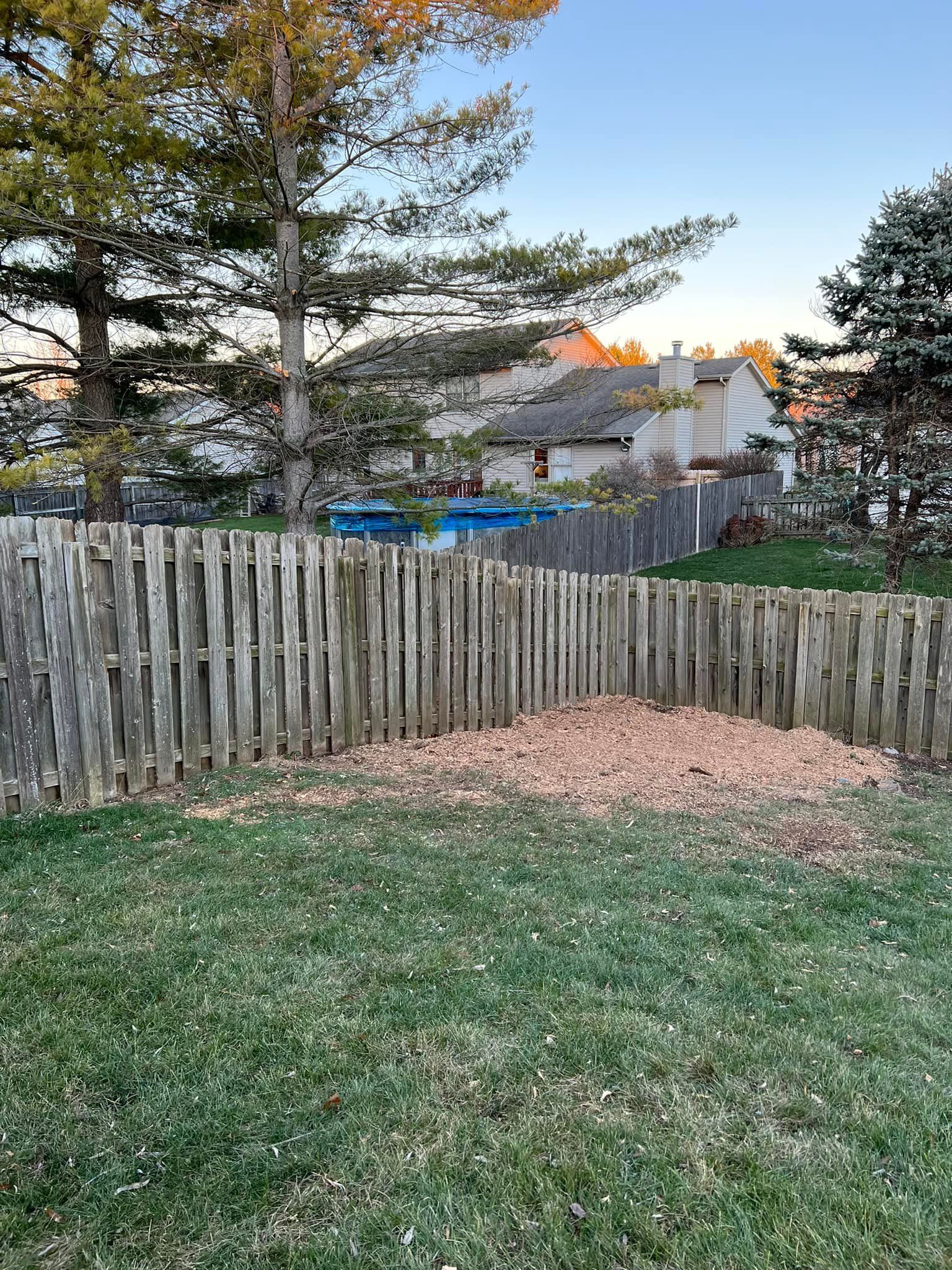 A wooden fence surrounds a lush green yard with a pool in the background.