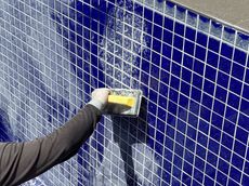 Person using a sponge to clean grout lines on blue tiled pool wall.
