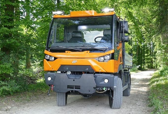 Un camioncino arancione di servizio su una strada sterrata forestale, visto frontalmente.
