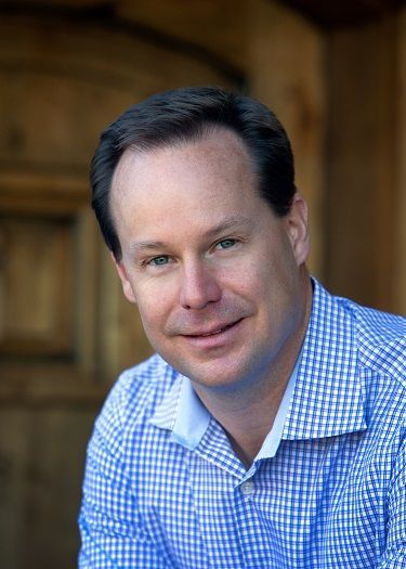 A man in a blue and white checkered shirt is smiling for the camera.