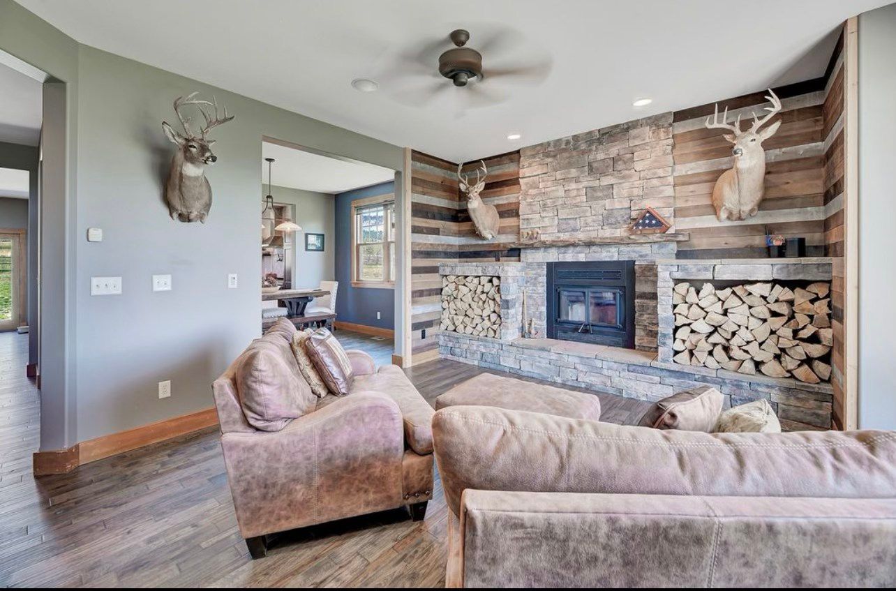 A living room with a fireplace , couch , chair and deer heads on the wall.