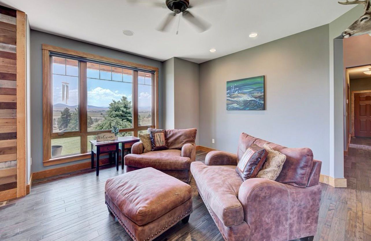 A living room with a couch , chair , ottoman and ceiling fan.