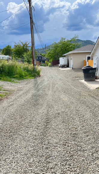A gravel road leading to a house with mountains in the background.