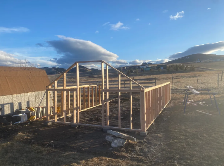 A greenhouse is being built in a field with mountains in the background.
