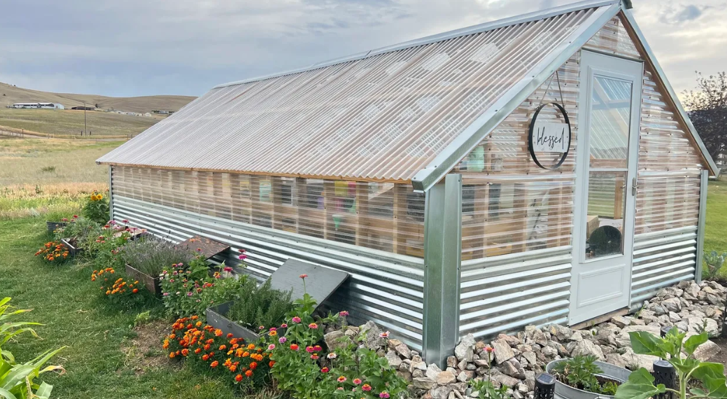 A greenhouse is sitting in the middle of a field surrounded by flowers.