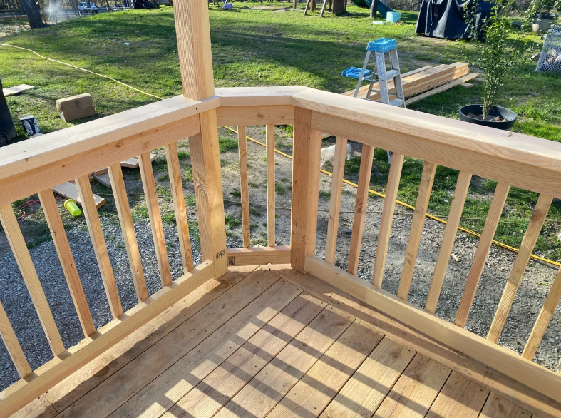 A wooden deck with a railing and a ladder in the background.