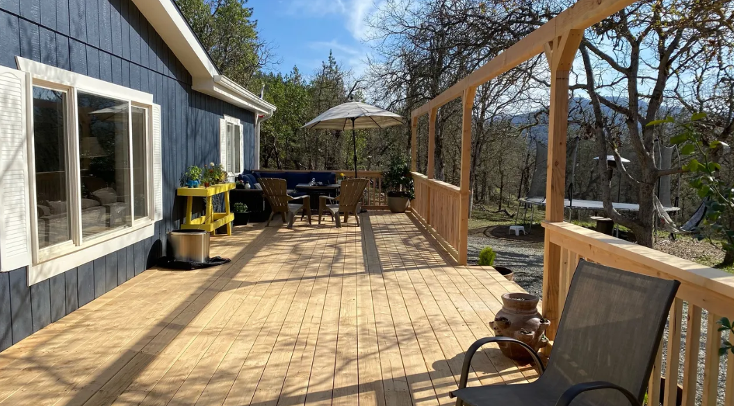 A large wooden deck with a chair and umbrella in front of a house.