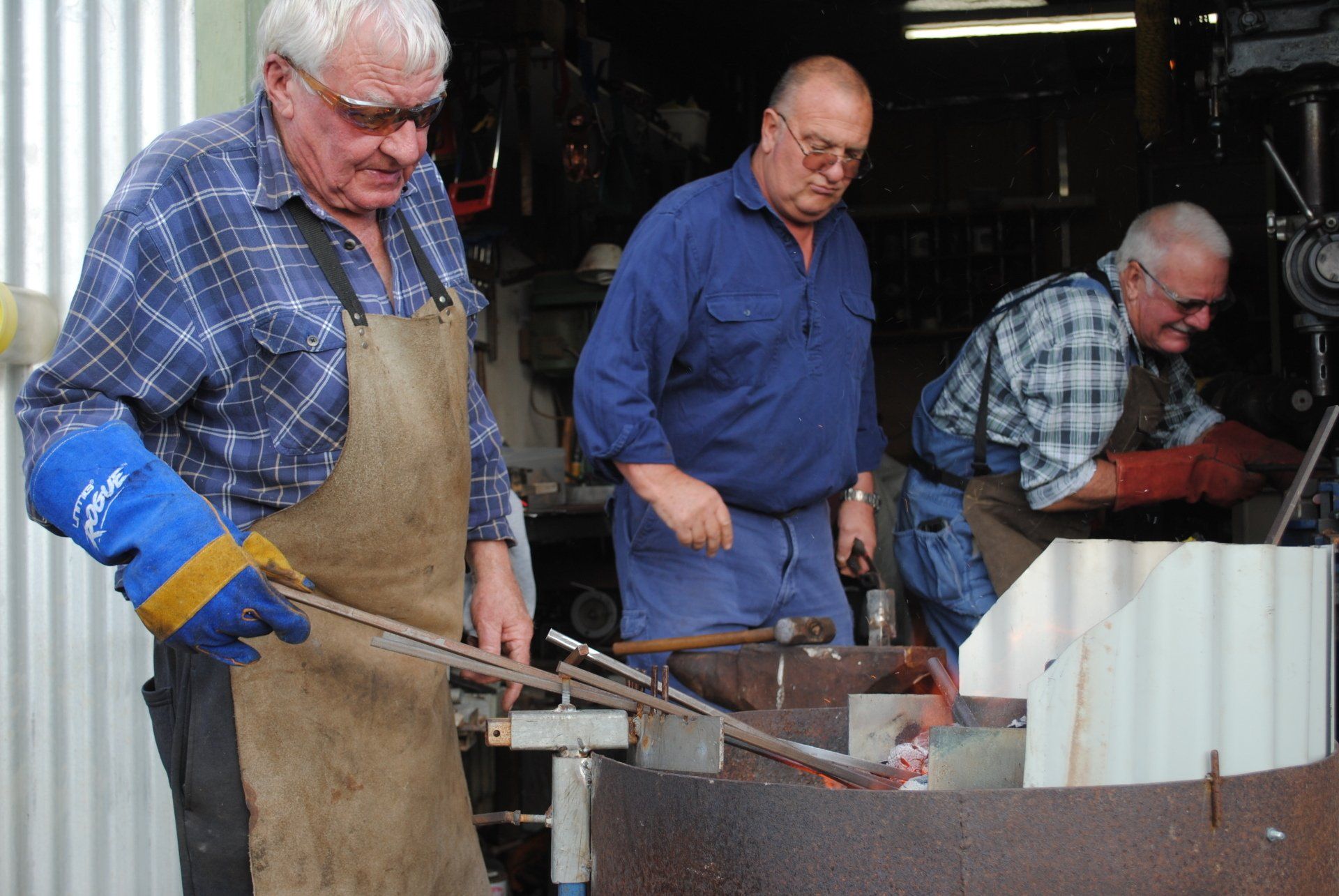 Three men work at a metal foundry, pouring molten metal into a mold.