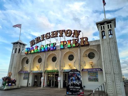Brighton Palace Pier entrance with sign, white and tan building, blue sky.