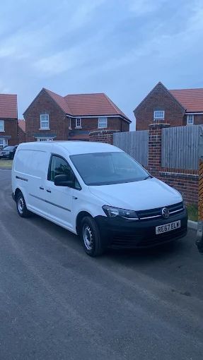 A white Volkswagen Caddy cargo van parked on a suburban street in front of brick houses.