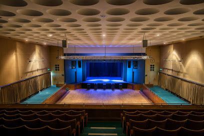Interior view of a theater stage with blue lighting, seating, and a unique, circular ceiling design.