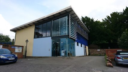 Modern building with glass front and blue and yellow walls; parked cars in front.