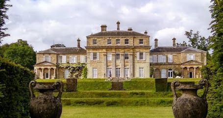 Grand stone mansion with symmetrical design, columns, and a terraced garden with urns.