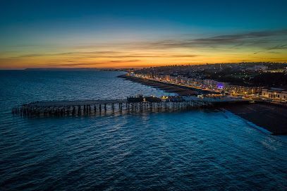 Ocean pier at dusk, with lights along the coast and colorful sky above the water.