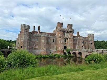 Red brick castle with turrets and a moat under a cloudy sky.