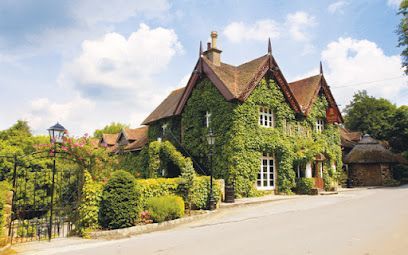 Ivy-covered cottage with thatched-roof extension, nestled on a road under a blue sky.