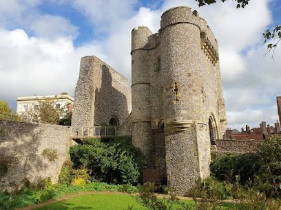 Ruined stone castle walls with two turrets, green foliage, blue sky.