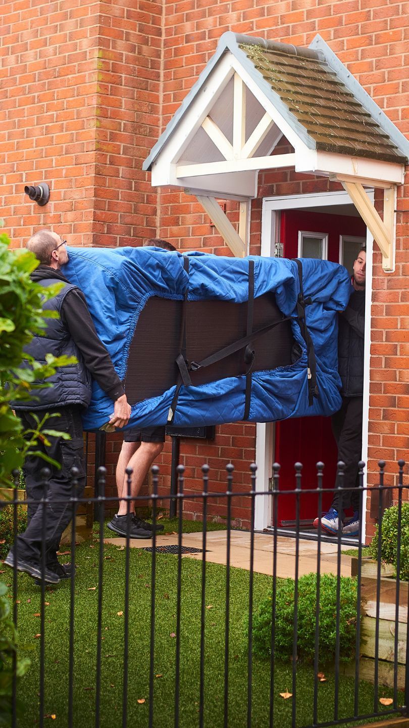 3 men carrying a sofa into a red brick house