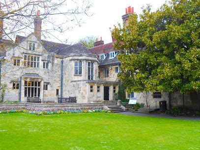 Stone manor house with a large green lawn, trees, and flower beds.