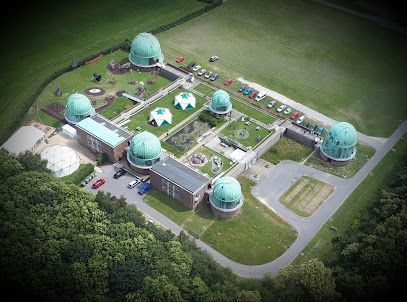 Aerial view of an observatory with multiple green-domed buildings on a green lawn with trees. Cars are parked nearby.
