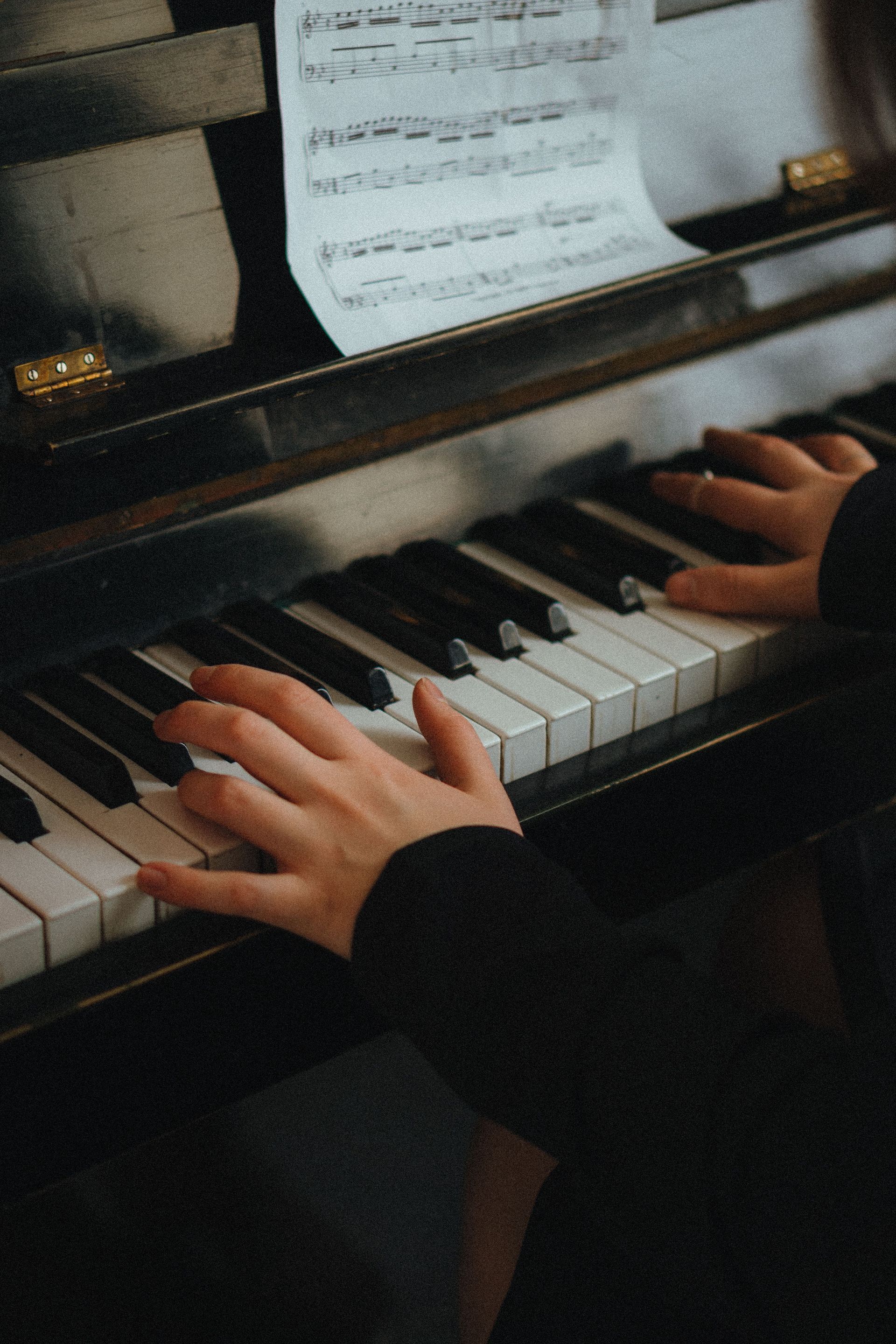 Hands playing sheet music on an upright piano.