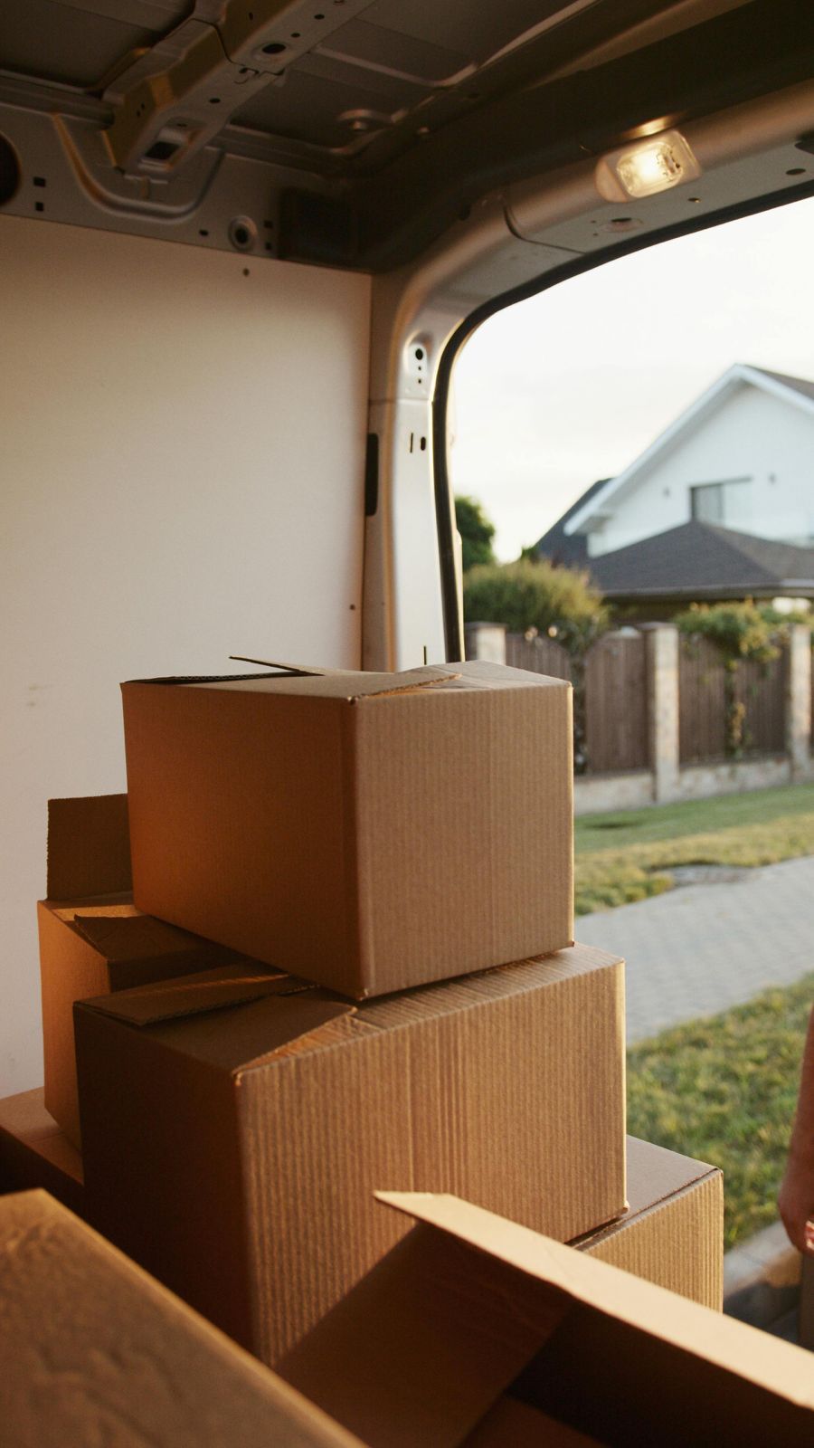 Stacked cardboard boxes inside a van with the open door showing a residential street