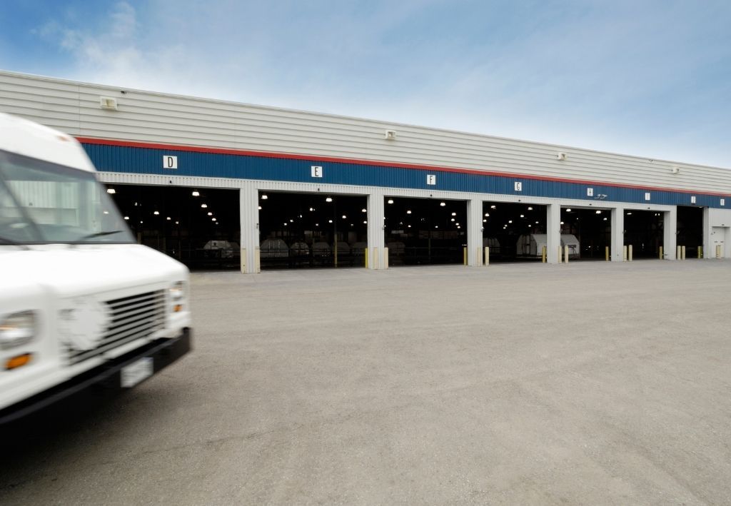 White delivery van in front of a long warehouse with multiple loading docks, under a blue sky.