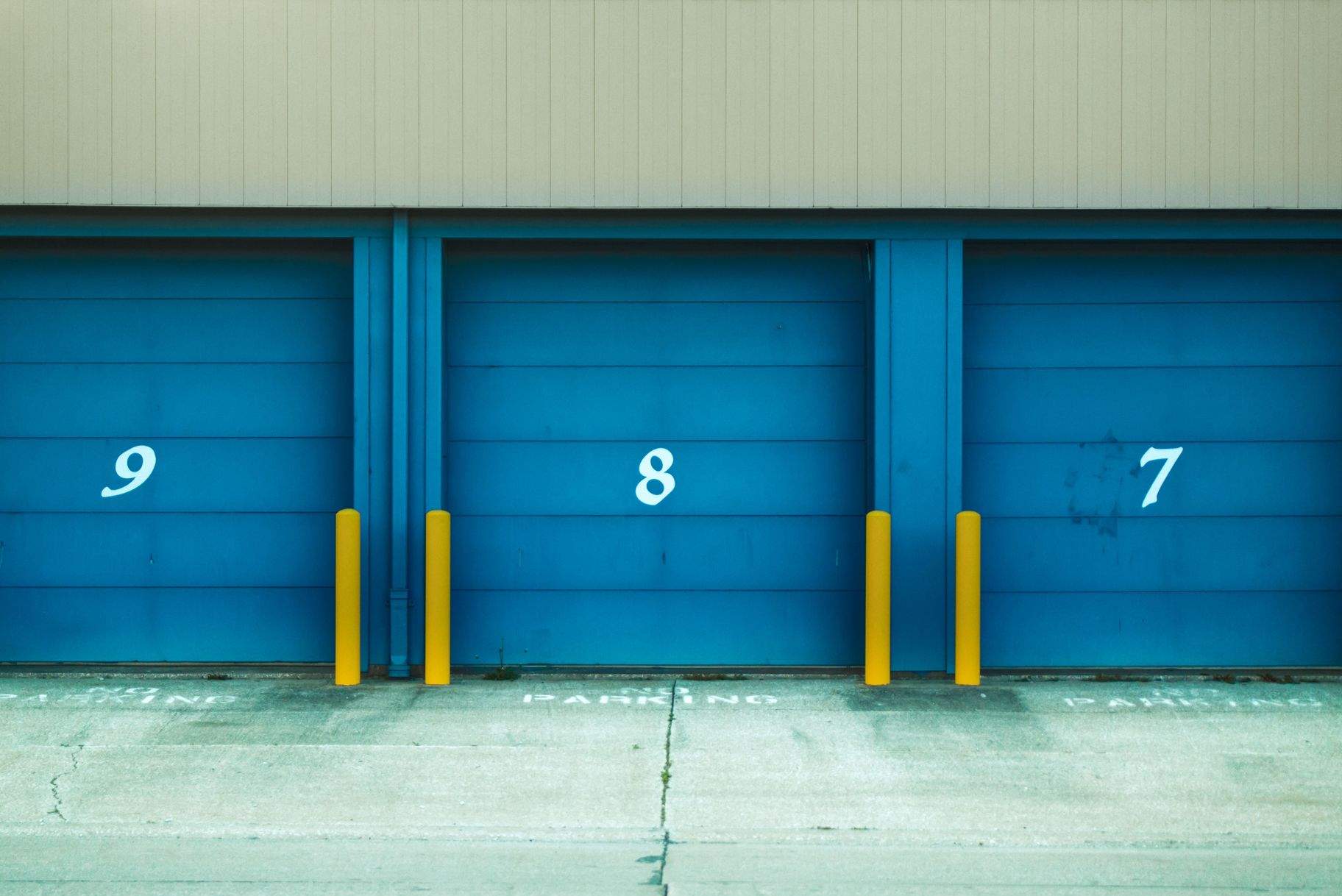 Three blue garage doors numbered 9, 8, and 7 with yellow bollards in front
